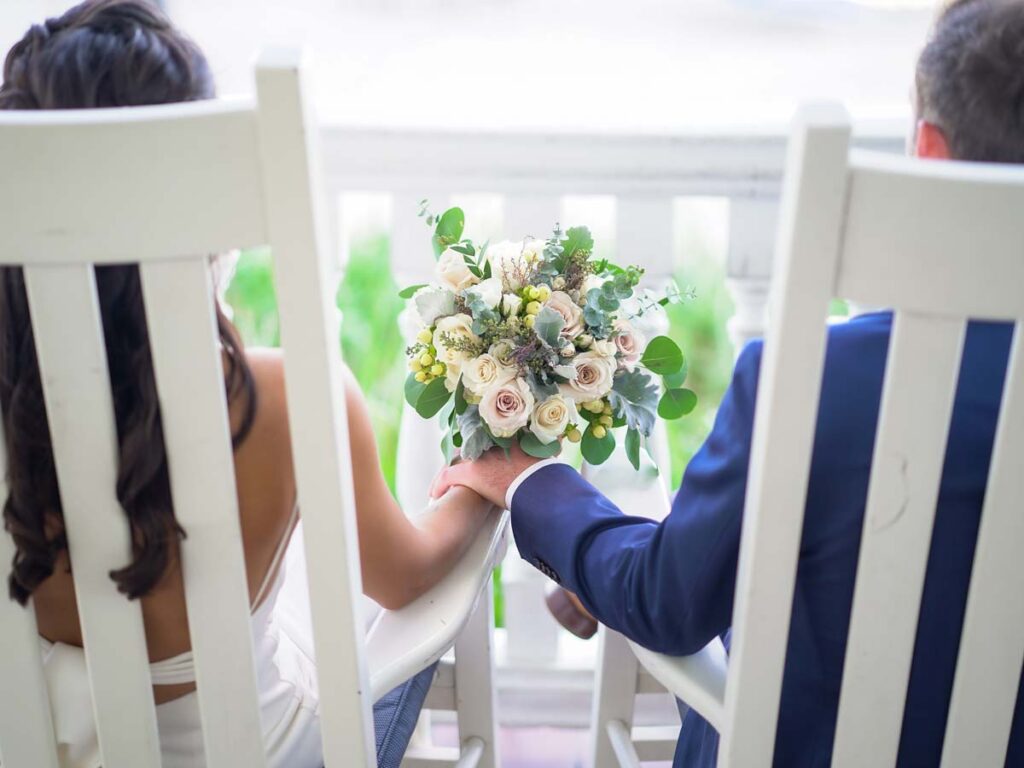 Bride And Groom Holding Hands In Rocking Chairs.